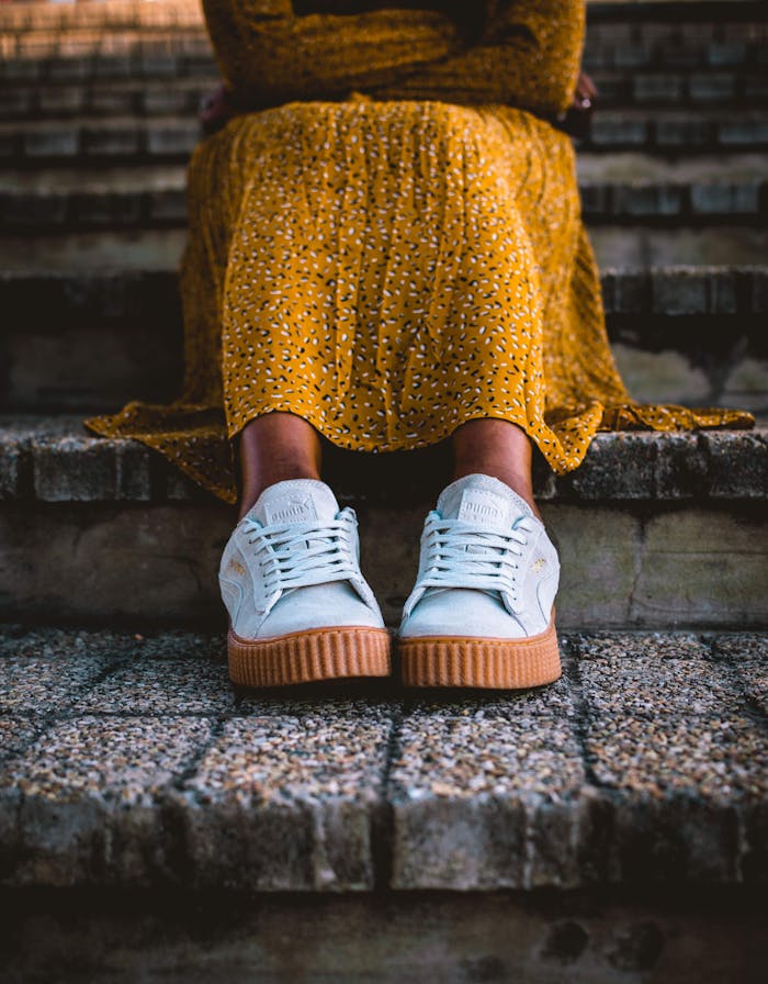 hero-img-01 A close-up shot of a woman in a yellow dress and white sneakers sitting on stone steps.